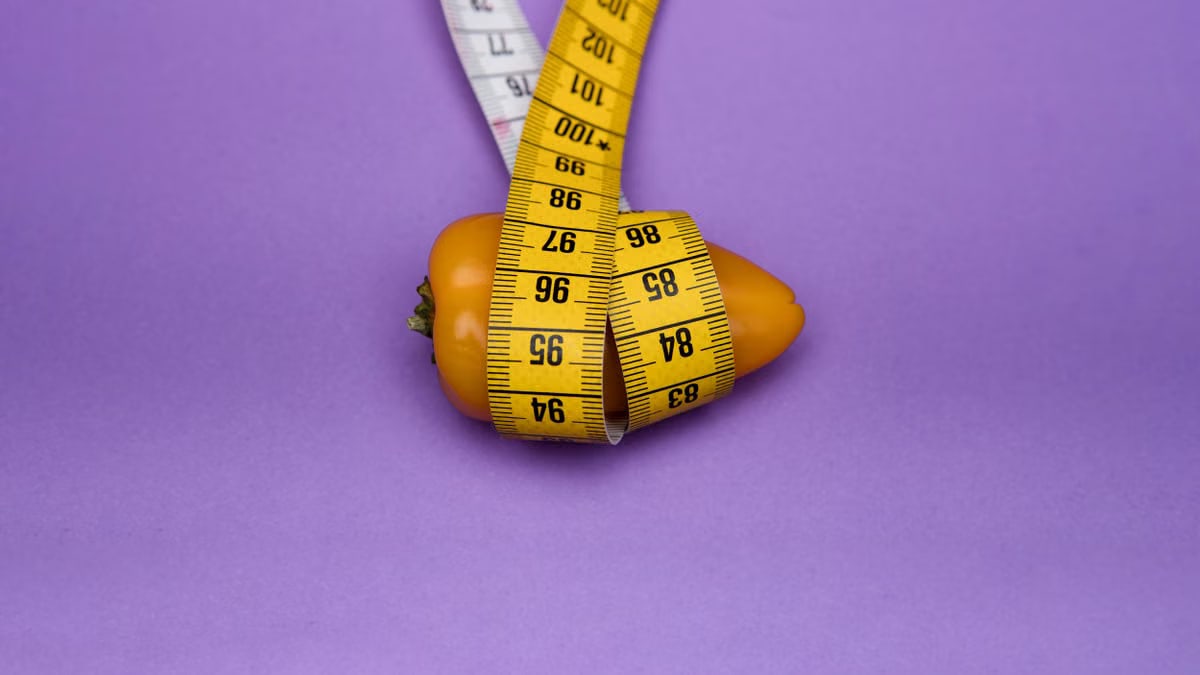 A yellow bell pepper wrapped in a yellow measuring tape against a purple background, symbolizing dieting and measurement.